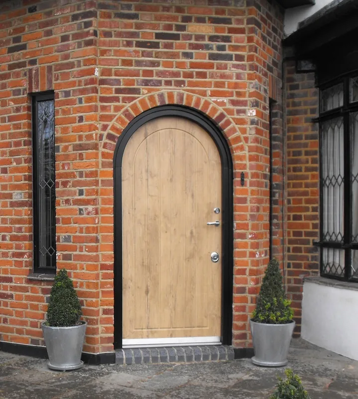Arched wood-style residential security door in a brick entry